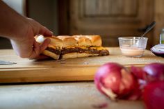 a person is cutting up a sandwich on a wooden board next to onions and garlic