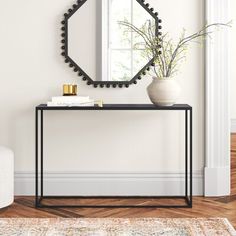 a black console table with a white vase and mirror on the wall in front of it