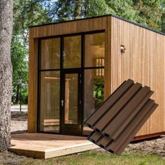 a small wooden structure with sliding glass doors in the grass and trees around it, next to a tree