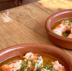 two brown bowls filled with soup and shrimp on top of a wooden table next to each other