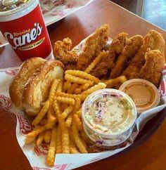 a basket filled with chicken and fries next to a cup of coleslaw on top of a table