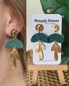 a pair of gold and green earrings with leaves hanging from the front, next to a photo of a woman's earring