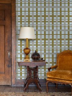 a chair and table in front of a wallpapered room with a lamp on it