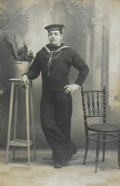 an old black and white photo of a sailor standing next to a chair