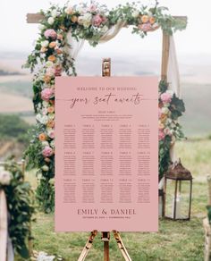 a pink wedding seating sign on a tripod with flowers and greenery in the background