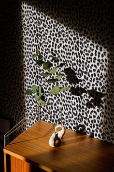 a vase sitting on top of a wooden table next to a wall covered in animal print