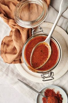 two jars filled with red sauce on top of a white plate next to a spoon