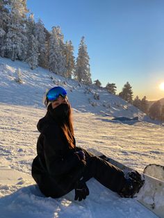 a person sitting in the snow with their feet on a snowboard and wearing goggles