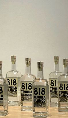 six bottles of tequila 818 are lined up on a table with white walls in the background