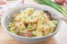 a bowl filled with potatoes and meat on top of a wooden table next to asparagus