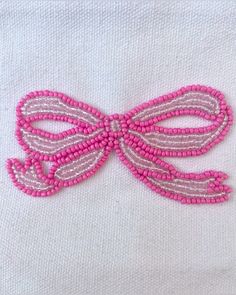 a white shirt with pink beads and a bow on it's chest, embroidered onto the front