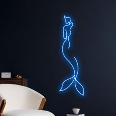 a room with a white chair and a blue neon mermaid wall decal on the wall