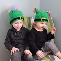 two young children sitting on a chair wearing matching knitted hats with pom poms