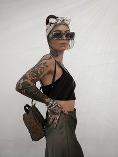 a woman with tattoos holding a purse and wearing sunglasses on her head while standing in front of a white wall