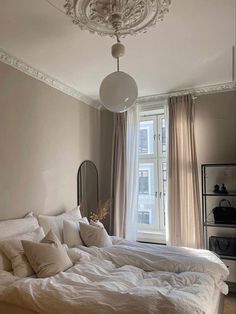 a bedroom with a bed, chandelier and large windows in it's corner