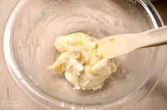 a wooden spoon in a glass bowl filled with batter and butter, on top of a table