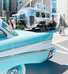 an old blue car parked in front of a building with a boat on it's roof