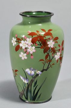 a green vase with red and white flowers painted on the side, sitting on a table