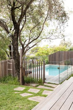 a wooden deck next to a pool surrounded by trees and grass with a fence around it