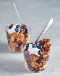 two cups filled with granola and blueberries on top of a table next to each other