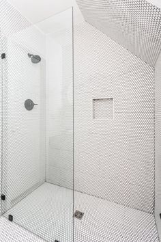 a white tiled bathroom with a glass shower door and black dots on the wall behind it