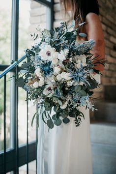 a woman in a white dress holding a large bouquet with blue and white flowers on it