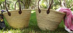 two woven baskets with handles are sitting in the grass, one has a pink towel on it