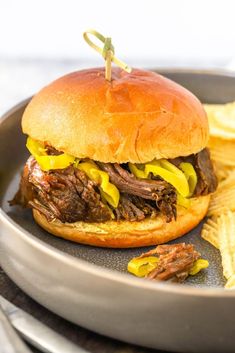 a roast beef sandwich with yellow peppers and mustard on a plate next to potato chips