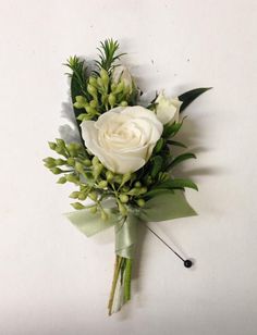 a boutonniere with white roses and greenery on the top is hanging from a wall