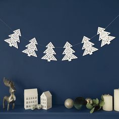 paper cut christmas trees are hanging on a string next to candles and other holiday decorations