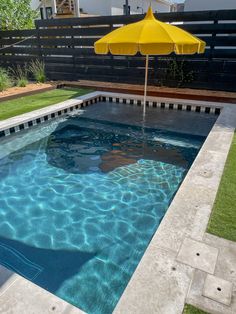 an empty swimming pool with blue water and yellow umbrella in the middle, surrounded by green grass