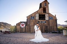 a bride and groom standing in front of a barn