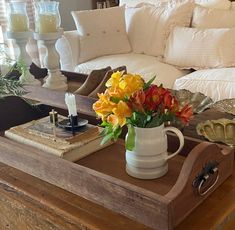 a coffee table with flowers and candles on it in front of a white couches