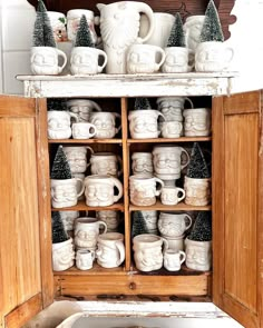 a cabinet filled with lots of white mugs next to wooden cupboards covered in christmas decorations