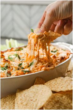 a hand holding a tortilla chip and dipping it into a casserole dish