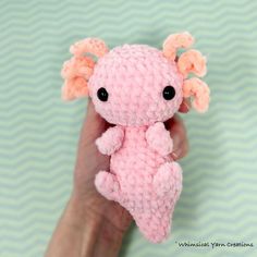 a small pink crocheted stuffed animal being held up by someone's hand