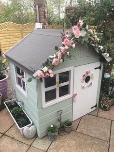 there is a small house with flowers on the roof and windows above it, along with potted plants