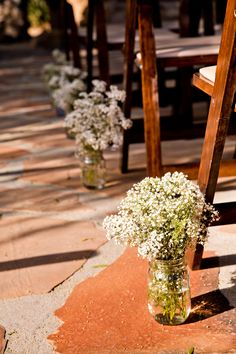 white flowers are in vases on the ground next to wooden chairs at an outdoor ceremony