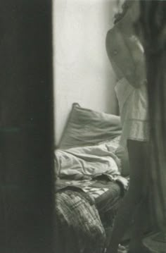 a shirtless man standing in front of a bed next to a window with curtains