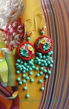 two pairs of colorful beaded earrings sitting on top of a striped cloth next to flowers