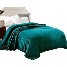 a bed covered in a green blanket next to a night stand