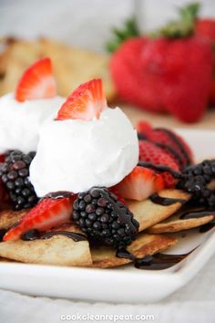 a white plate topped with fruit and whipped cream on top of crackers next to strawberries