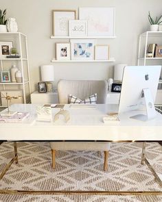 a white desk topped with a computer monitor next to a shelf filled with books and pictures