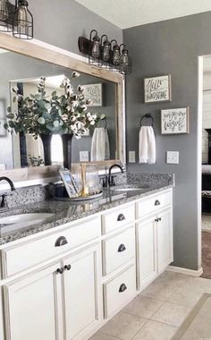 a white bathroom with gray walls and marble counter tops is decorated with vases filled with flowers