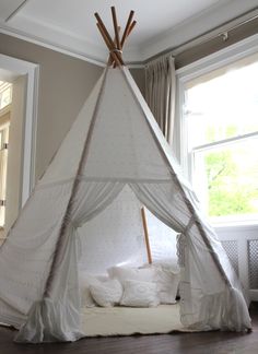 a white teepee sitting on top of a wooden floor next to a window in a room