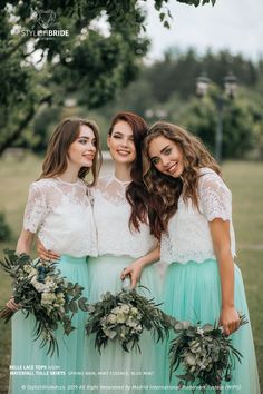 three beautiful young women standing next to each other in front of a tree and grass field