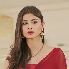 a woman in a red dress with long dark hair and large gold earrings on her head