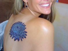 a woman with a blue flower tattoo on her shoulder and chest smiling at the camera