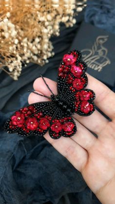 a woman's hand holding a red and black butterfly brooch