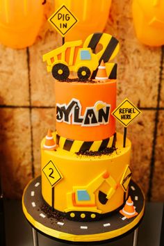 Orange and yellow two tiered kid's birthday cake with tractors, front loaders and construction cones and signs with a road surrounding the bottom tier. Dump Truck Birthday Cake, Dump Truck Cakes, Truck Birthday Cakes, Ben Ben